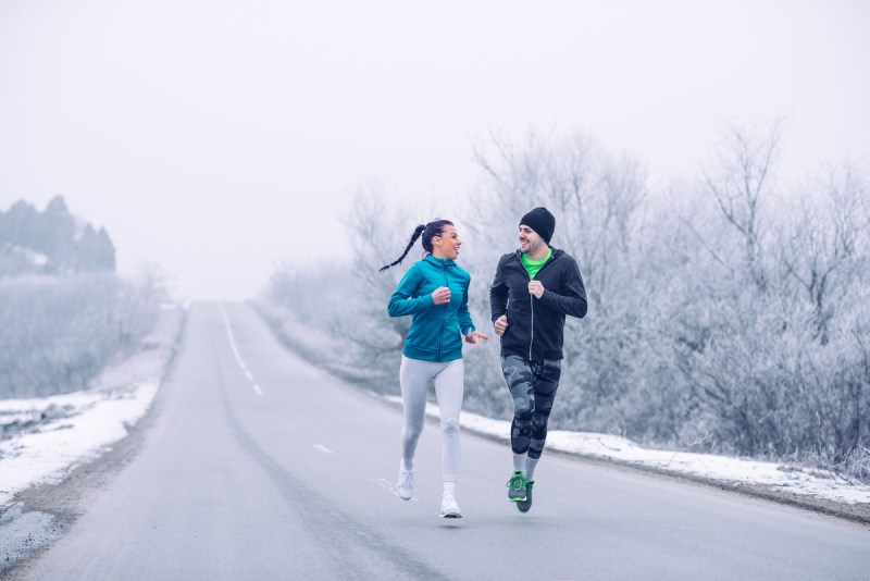 A man and woman running on a snowy winter road