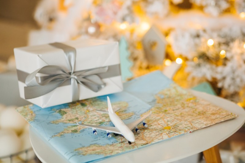 Small toy plane on world map in front of Christmas tree and wrapped present