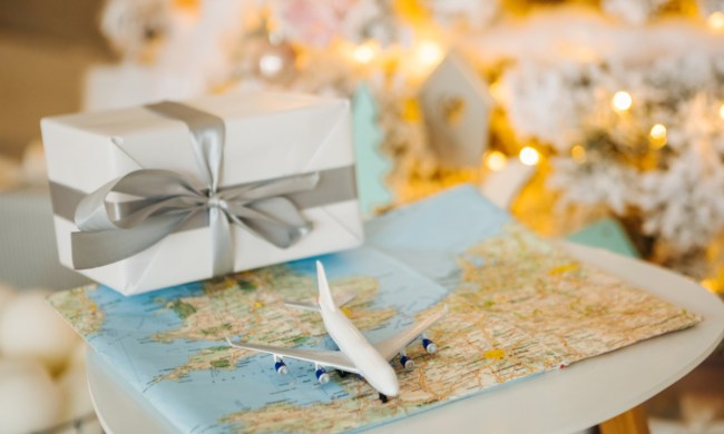Small toy plane on world map in front of Christmas tree and wrapped present