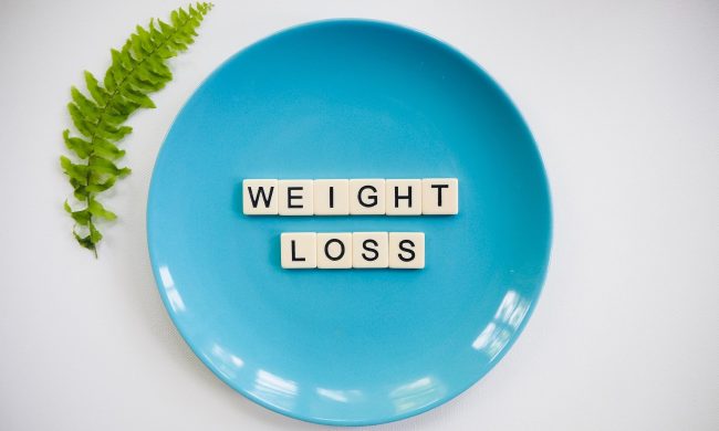 Blue plate with word blocks text weight loss on white background with green leaf