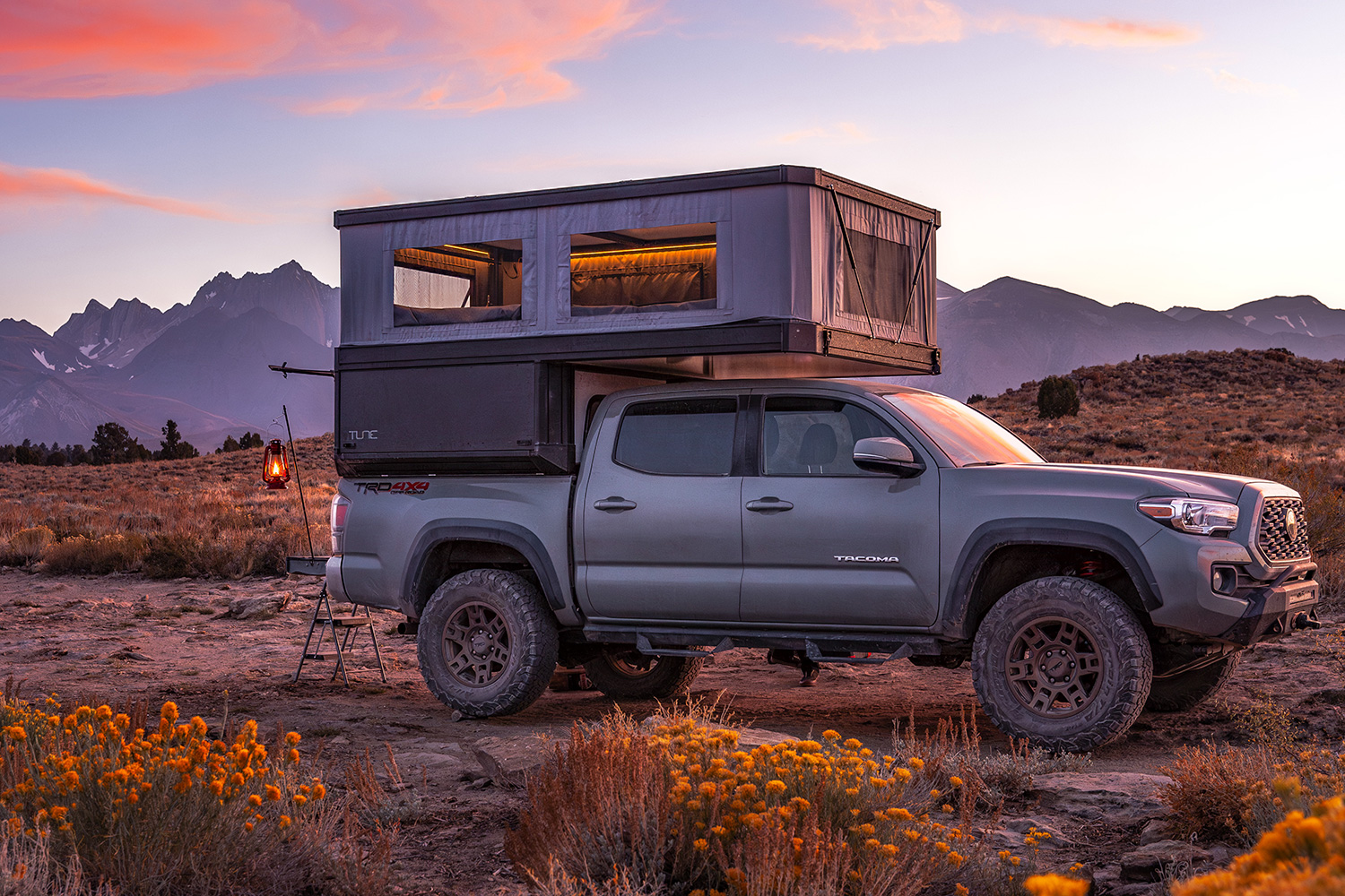 Toyota Tacoma with a Tune Outdoor M1 truck camper canopy parked in a field at sunset.