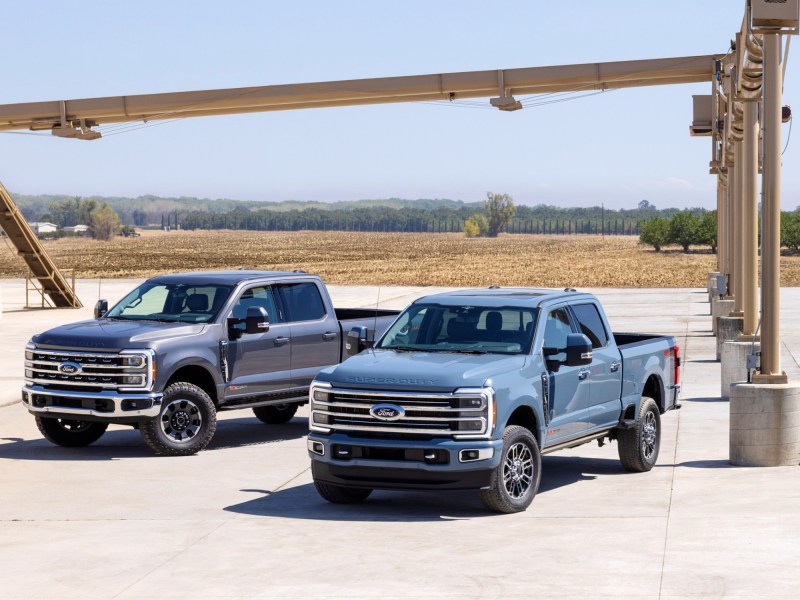 2023 Ford Super Duty F-250 Tremor Off-Road Package and F-350 Limited trucks on a worksite parked under an elevated sand conveyer.