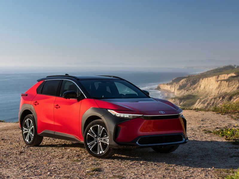 2024 Toyota bZ4X Limited AWD SupersonicRed parked on a cliff top with ocean below.