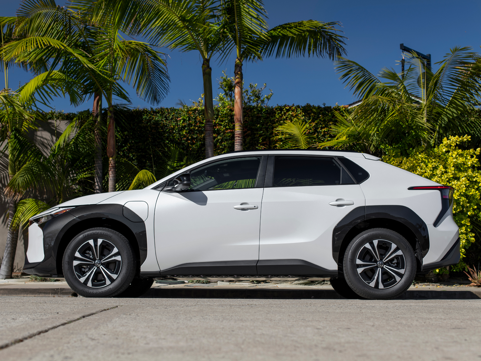 2024 Toyota bZ4X XLE FWD WindChillPearl parked on a street with palm trees in the background.