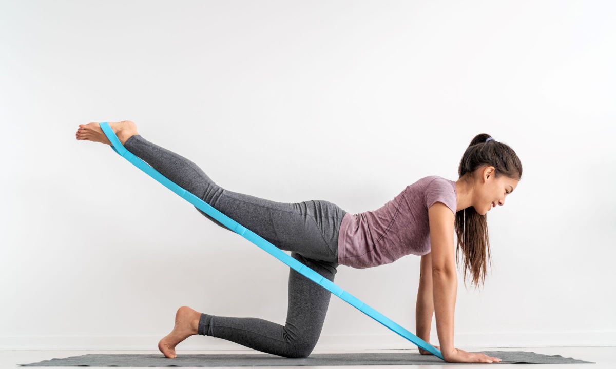 Woman doing donkey kickback or bird dog Pilates using a resistance band indoors
