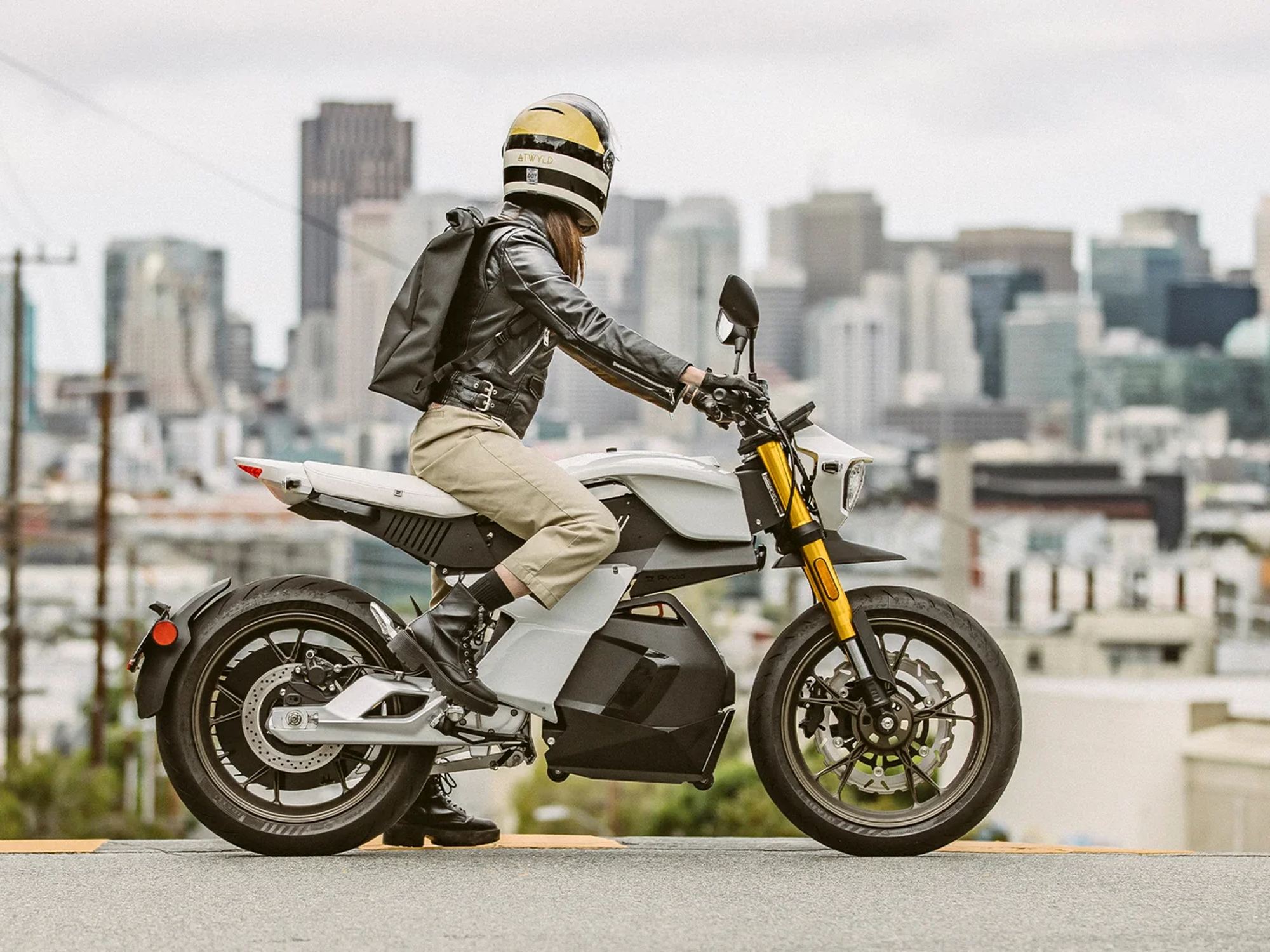Rider on a Ryvid Anthem electric motorcycle stopped on a street, overlooking a city.