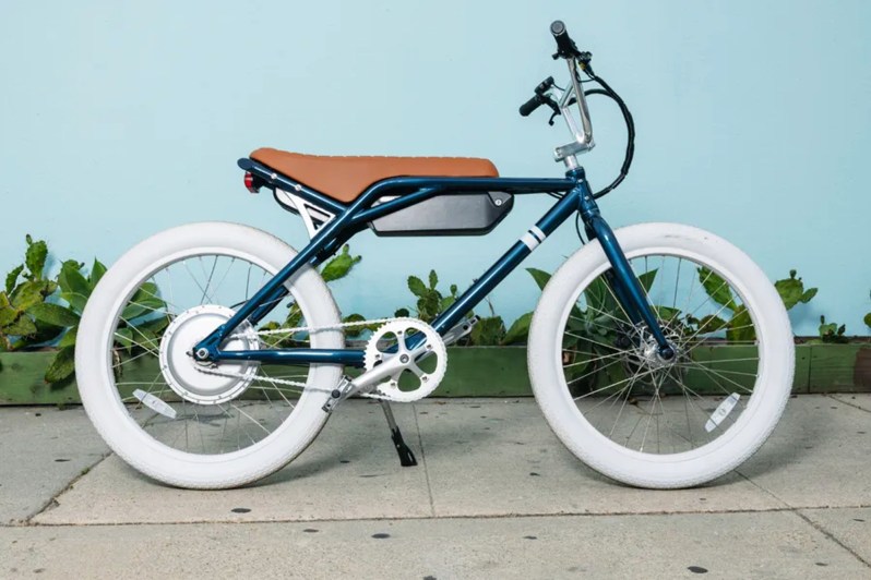 Sole e-24 e-bike in the Whaler colorway parked on a sidewalk with a light blue background.