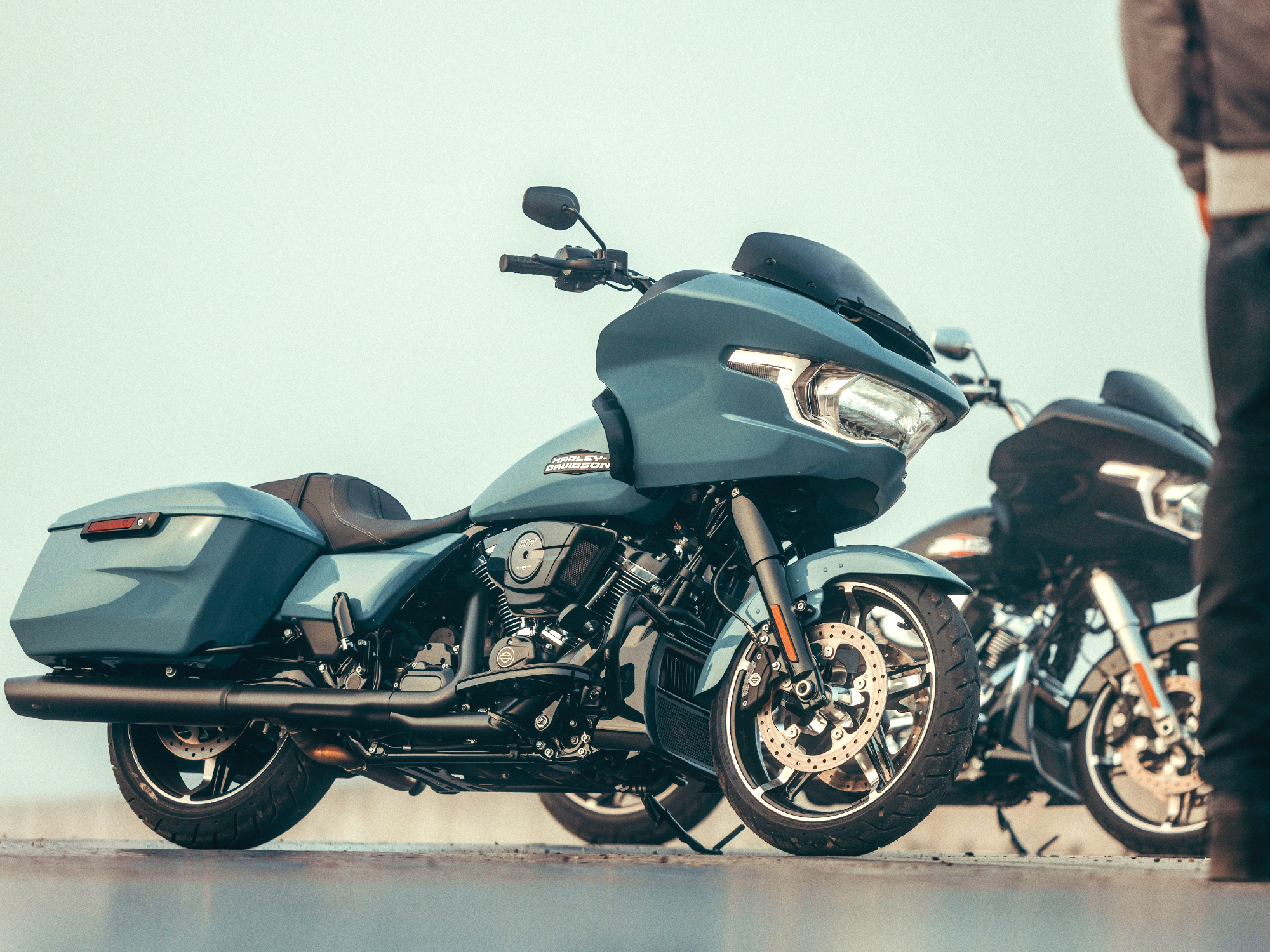 Two 2024 Harley Davidson Road Glides parked on concrete with a person standing on the right margin of the frame.