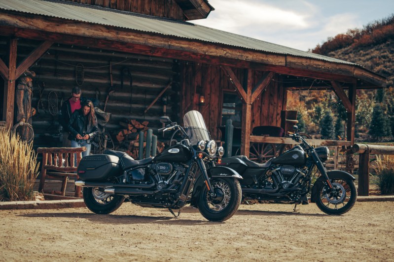 Two people in front of a log building getting ready to ride 2024 Harley-Davidson touring motorcycles.