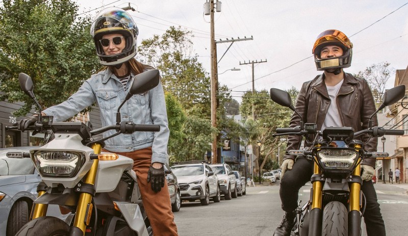 Two riders on Ryvid Anthem electric motorcycles stopped on a city street facing the camera.