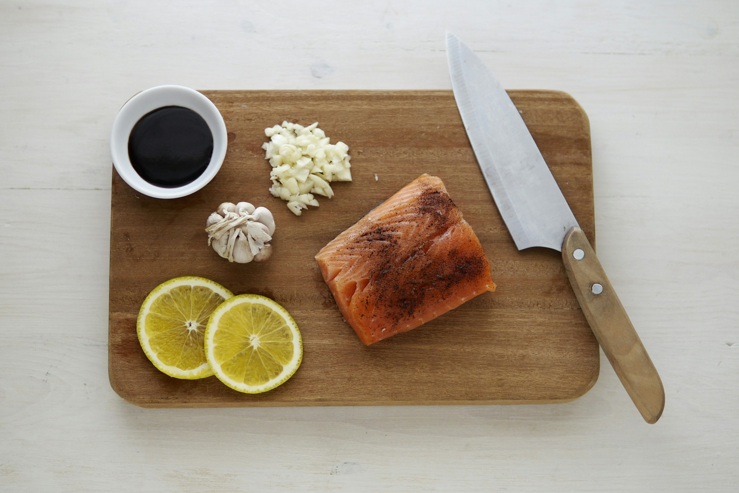 Salmon and lemon and garlic and cheese and knife on a wooden cutting board
