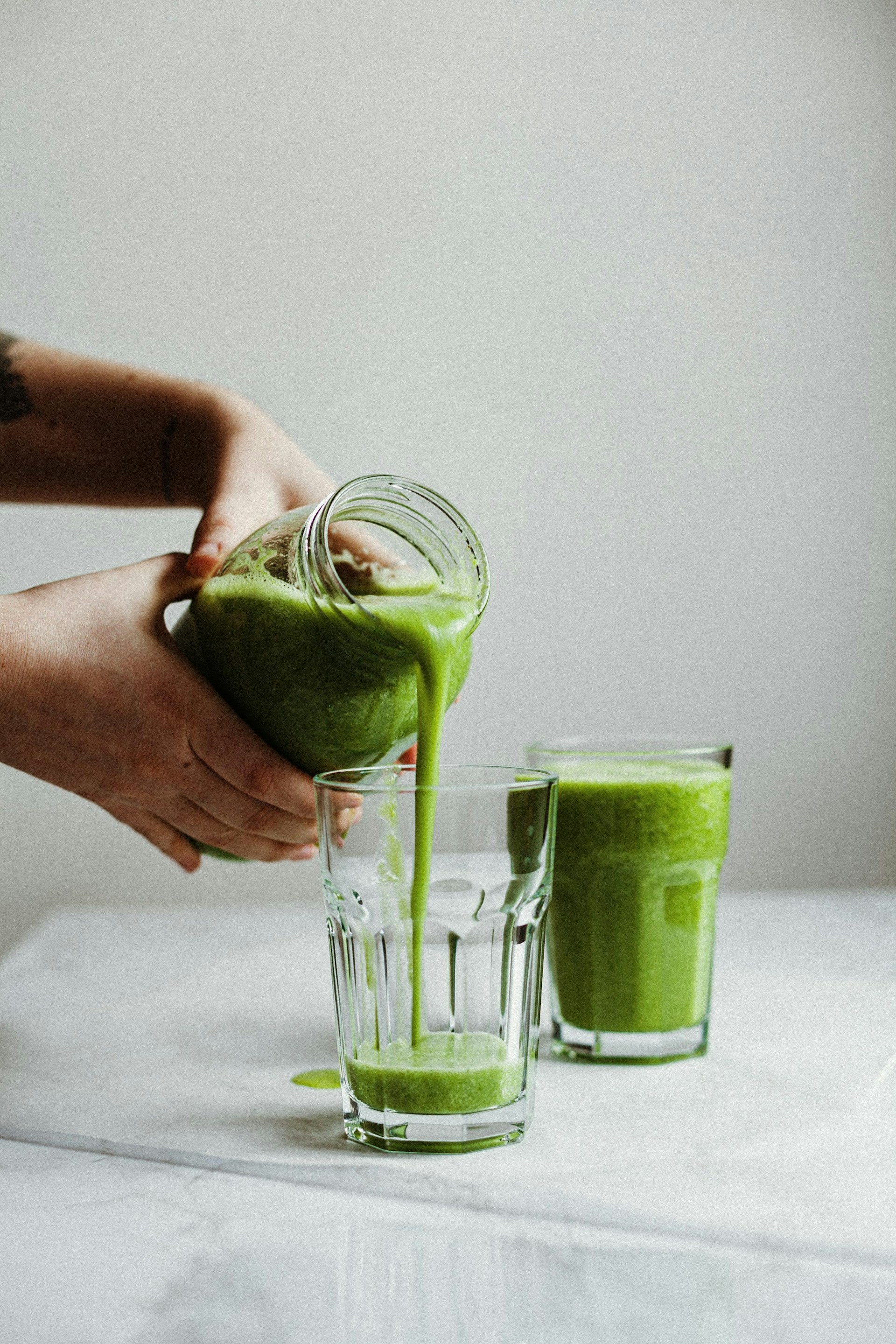 close up of someone hands pouring a green drink celery juice into a cup on a white table