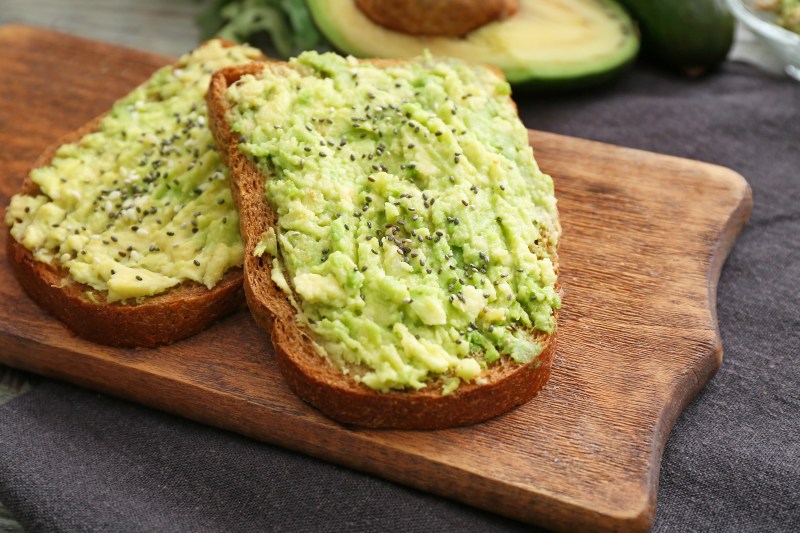 Tasty avocado toasts on wooden board