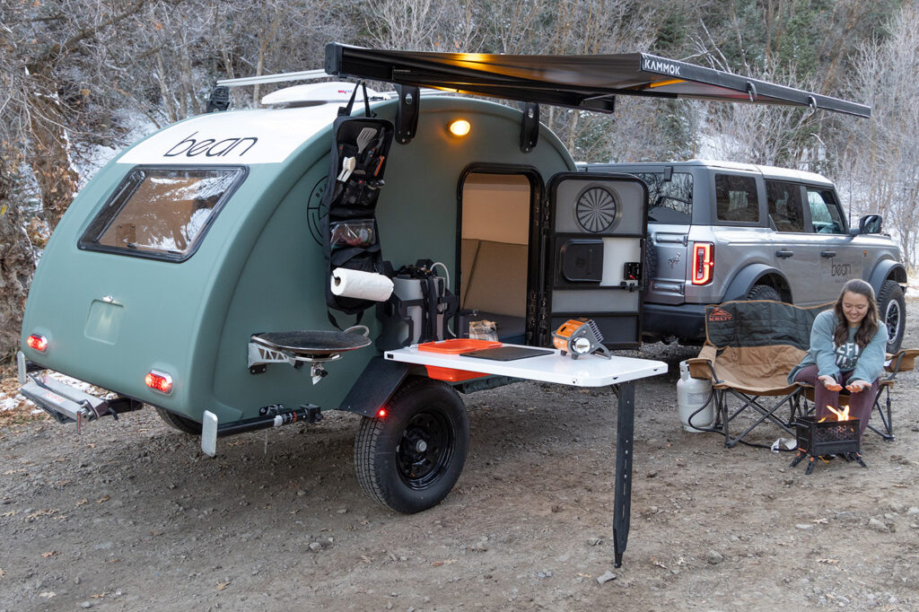 Woman solo camping outside a Bean Stock 2.0 teardrop travel trailer.