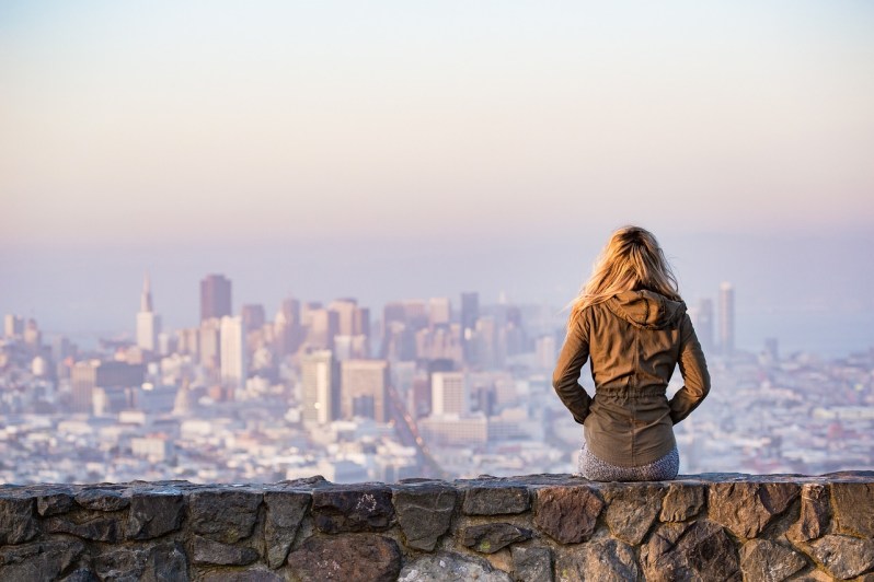 Blonde girl sitting on wall overlooking city