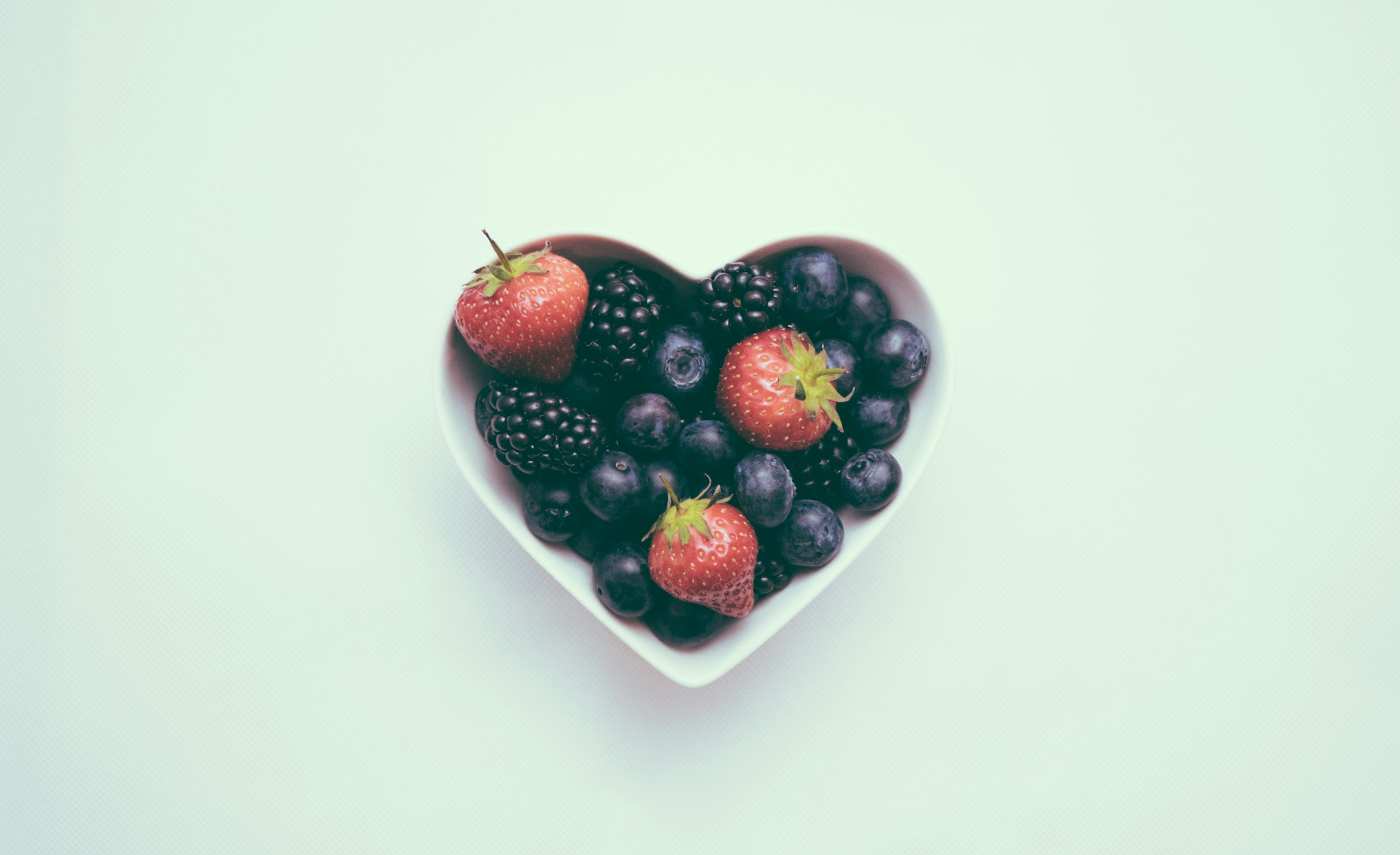 Berries in heart-shaped white container bowl with light green background