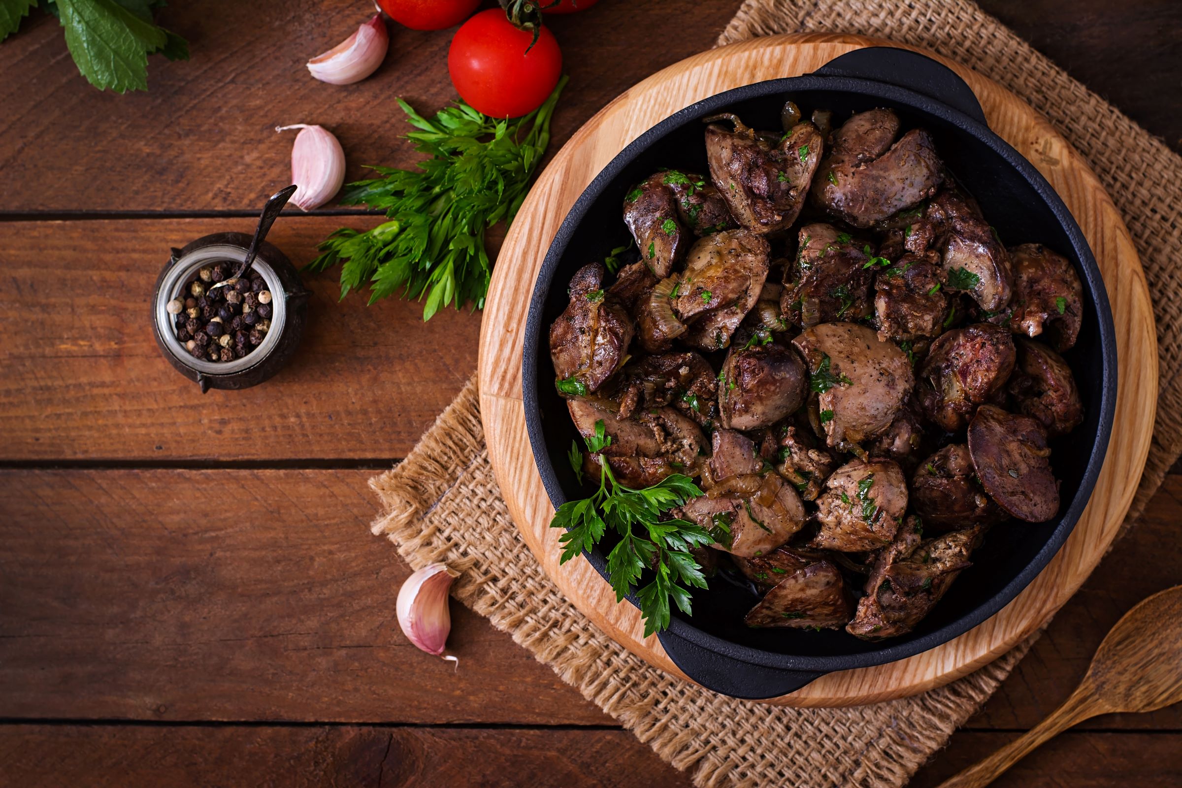 liver and onion on skillet on wood on table next to onions and herbs