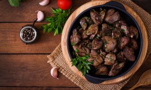 liver and onion on skillet on wood on table next to onions and herbs