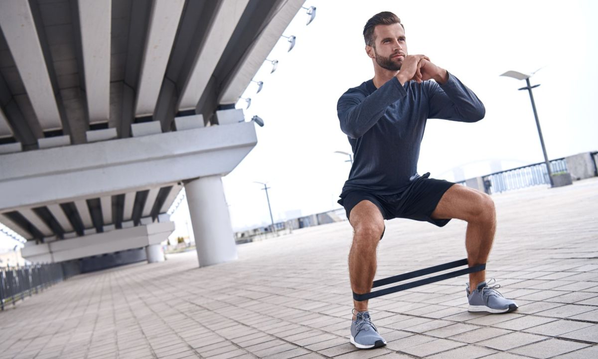 Young sportive man uses resistance band for exercising outdoors