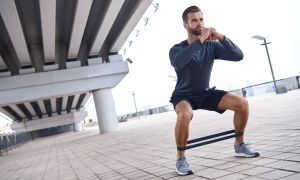 Young sportive man uses resistance band for exercising outdoors