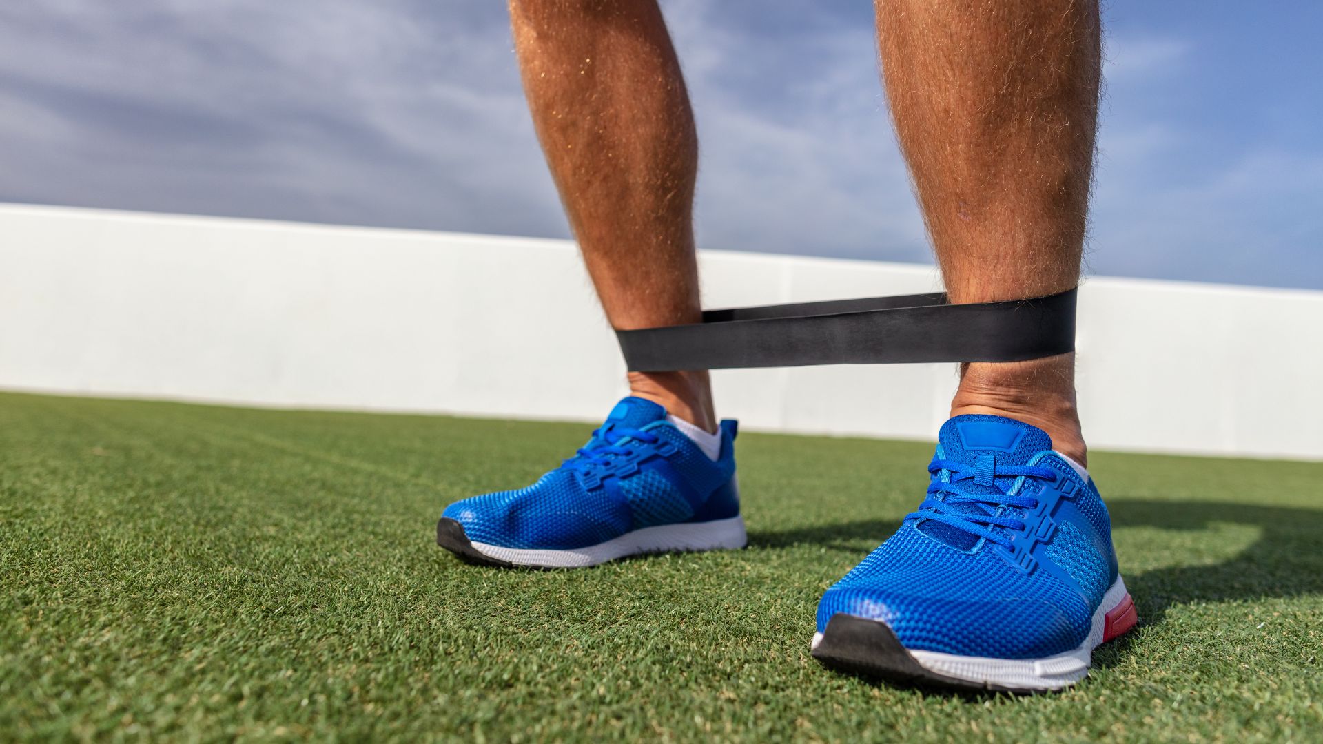 Man wearing resistance band on his ankle in blue tennis shoes