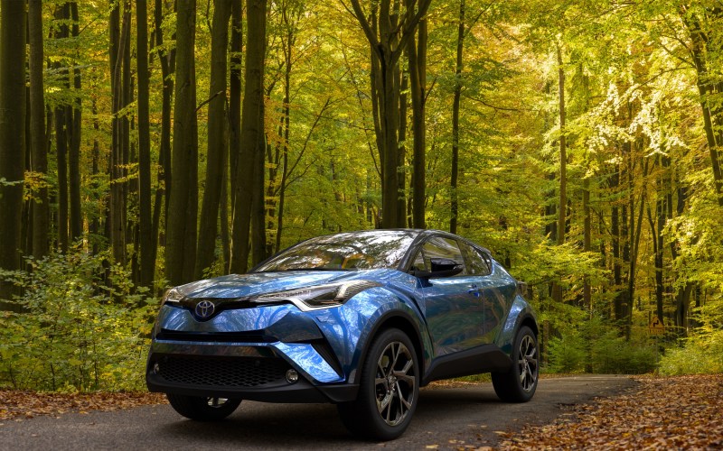 hybrid Toyota C-HR crossover SUV on a road leading through the autumn forest