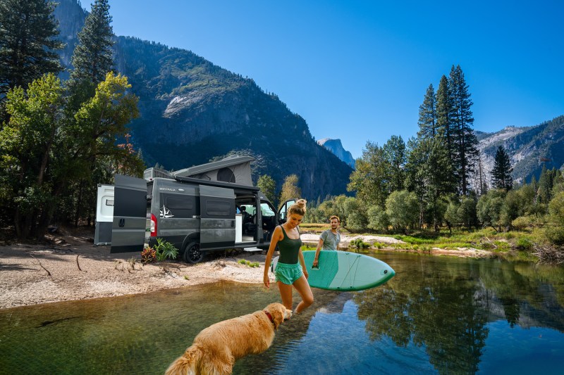 Young couple stepping into mountain stream with Westfalia Wave van in the background.