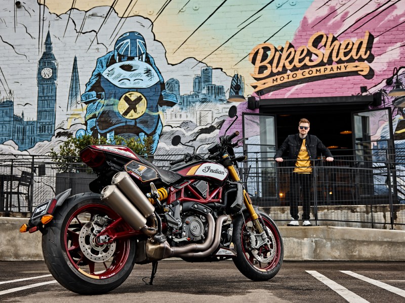 2024 Indian FTR x RSD Super Hooligan parked in front of Bike Shed store with a person leaning against metal fence looking directly at the camera.