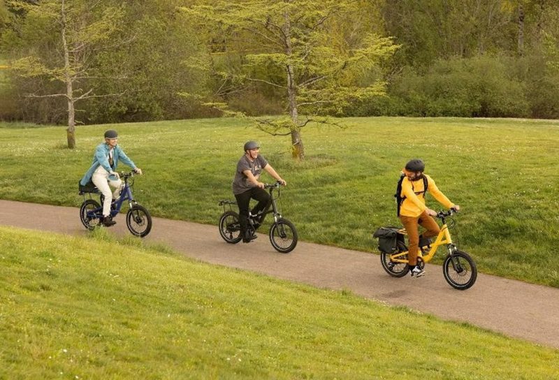 A group of people ride Co-op Cycles Generation e1.1 Electric Bikes through a park.