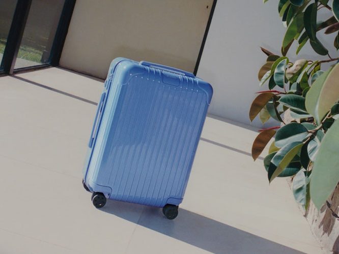 The Rimowa Sea Blue luggage placed next to a plant outside.