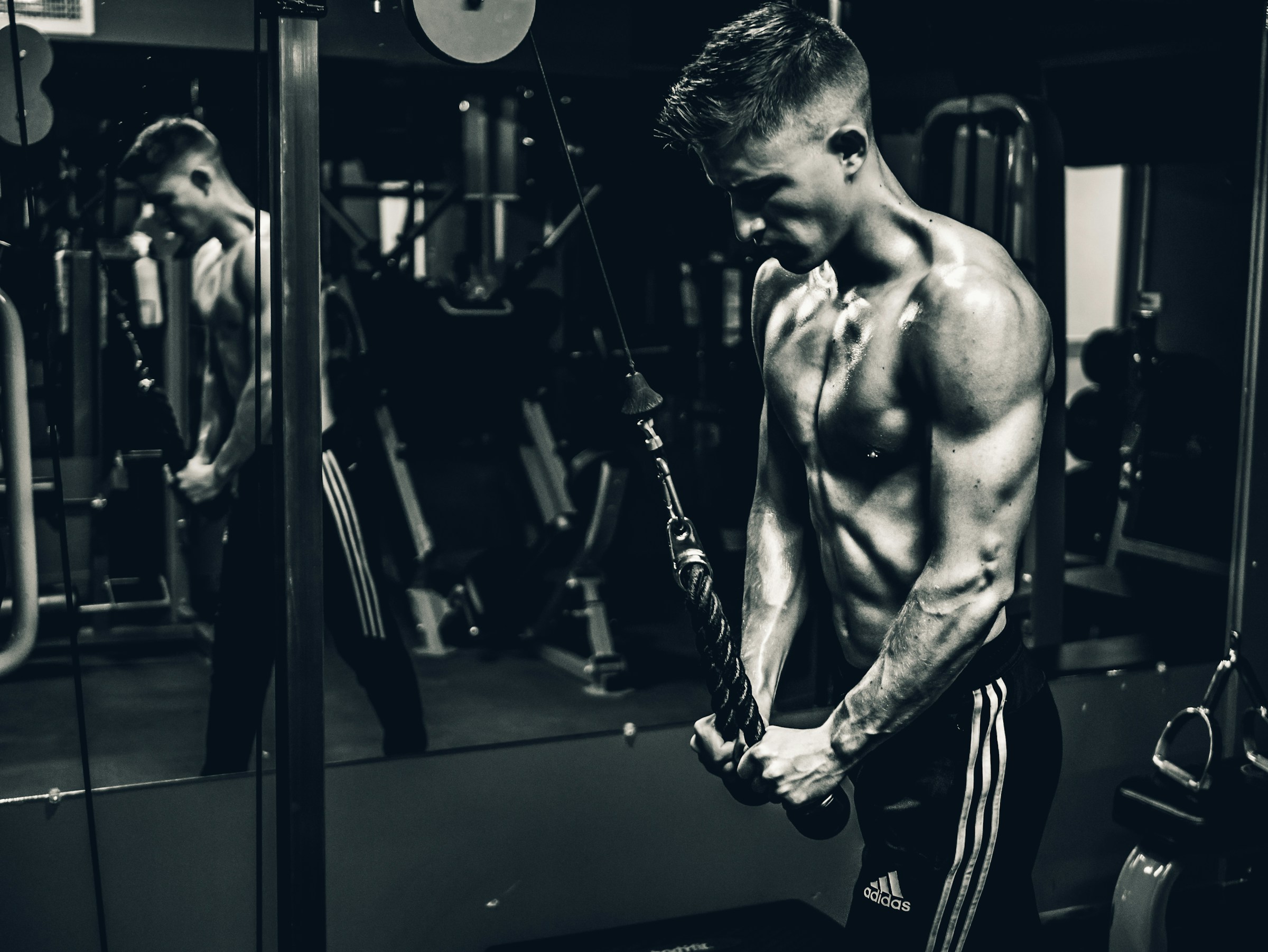 Black and white picture man shirtless doing cable pushdown exercise in the gym