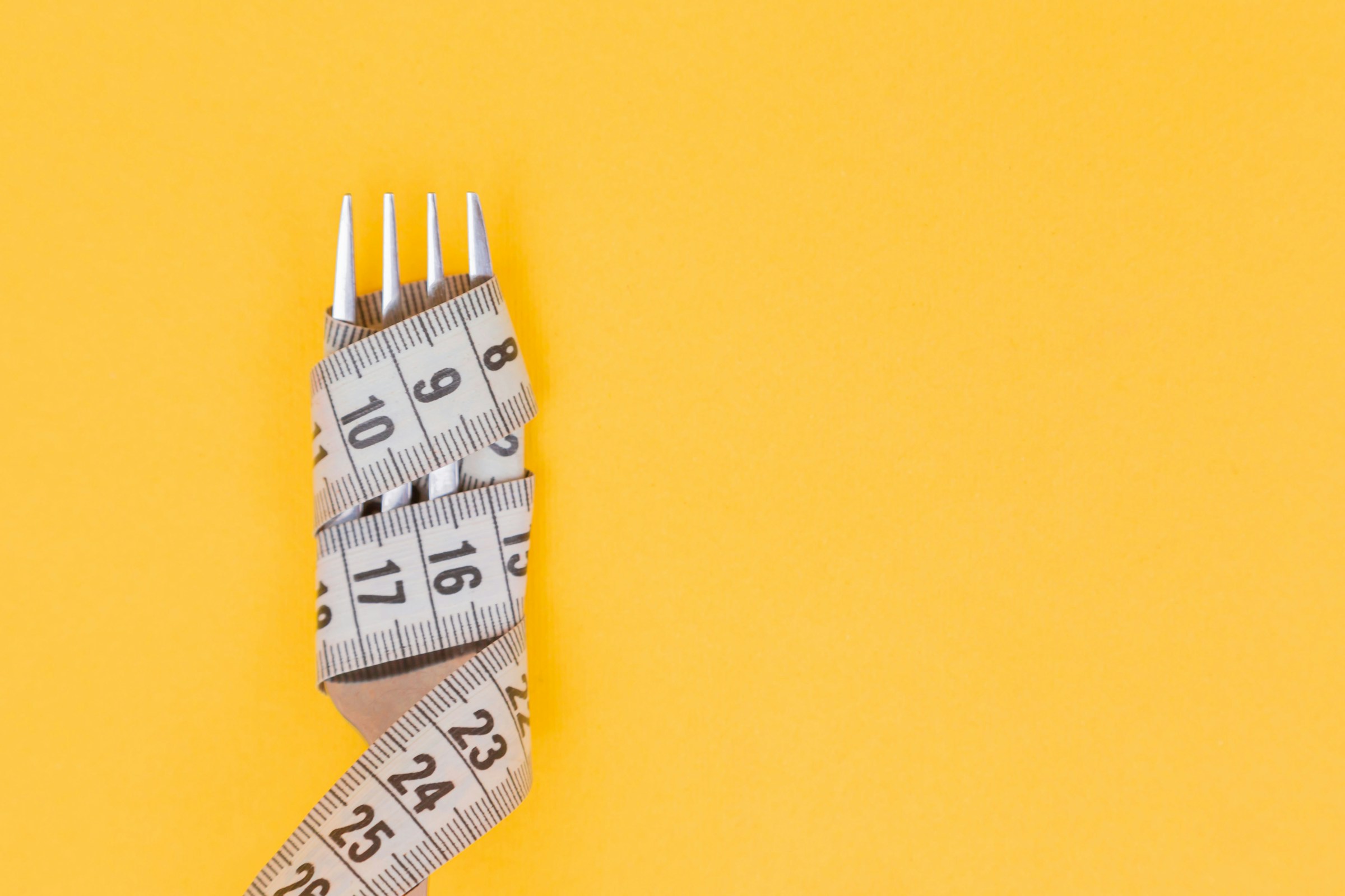 measuring tape wrapped around a silver fork on orange background