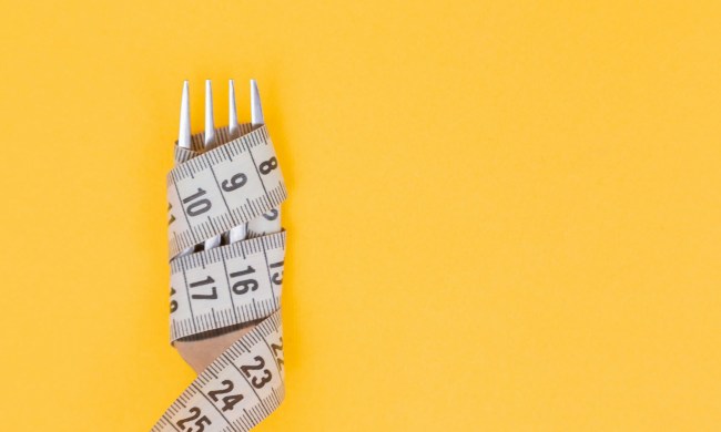 measuring tape wrapped around a silver fork on orange background