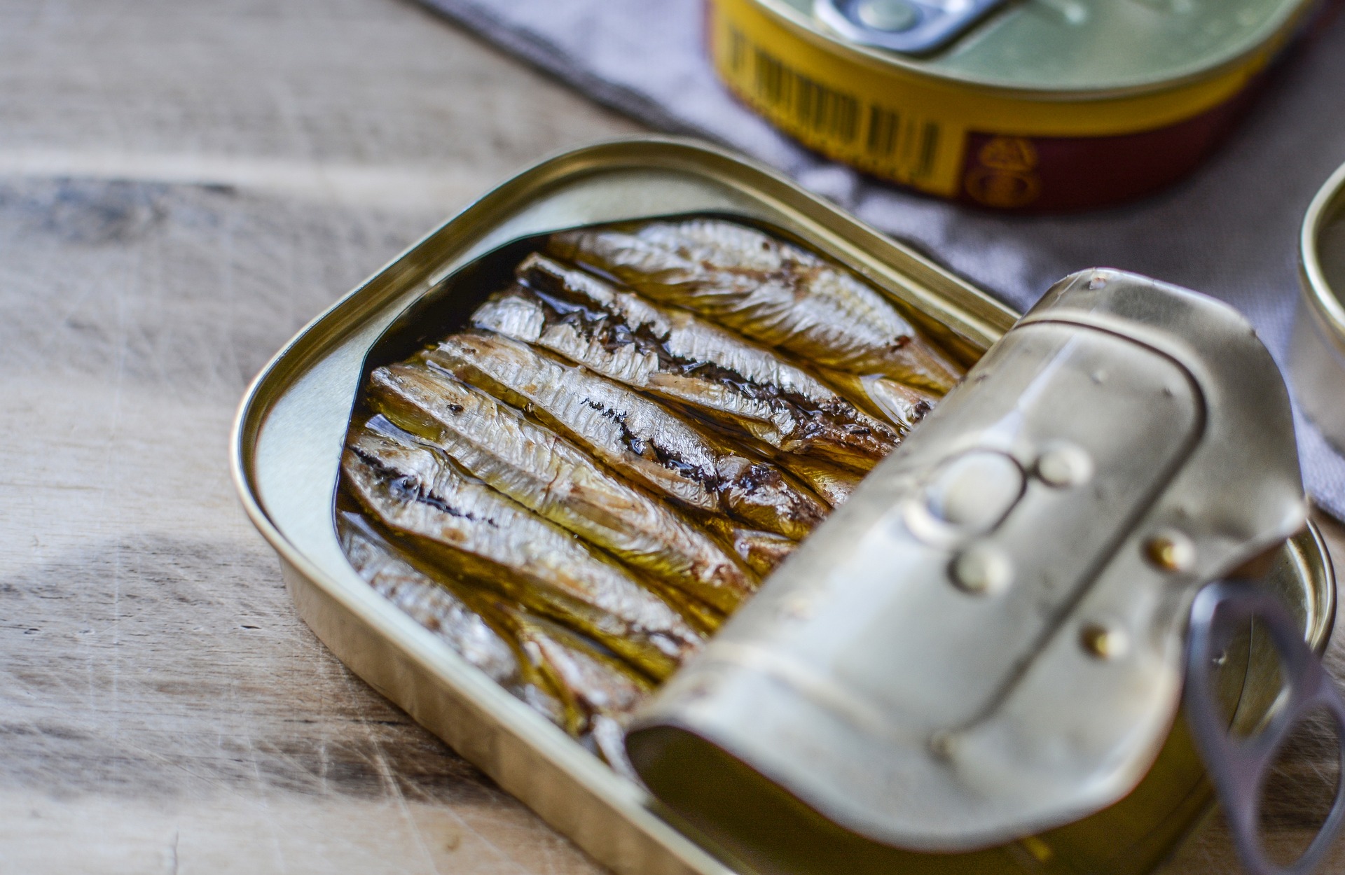 Half open can of sardines in oil on a wooden table