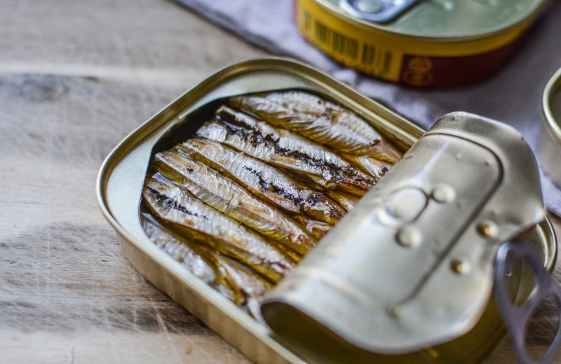 Half open can of sardines in oil on a wooden table
