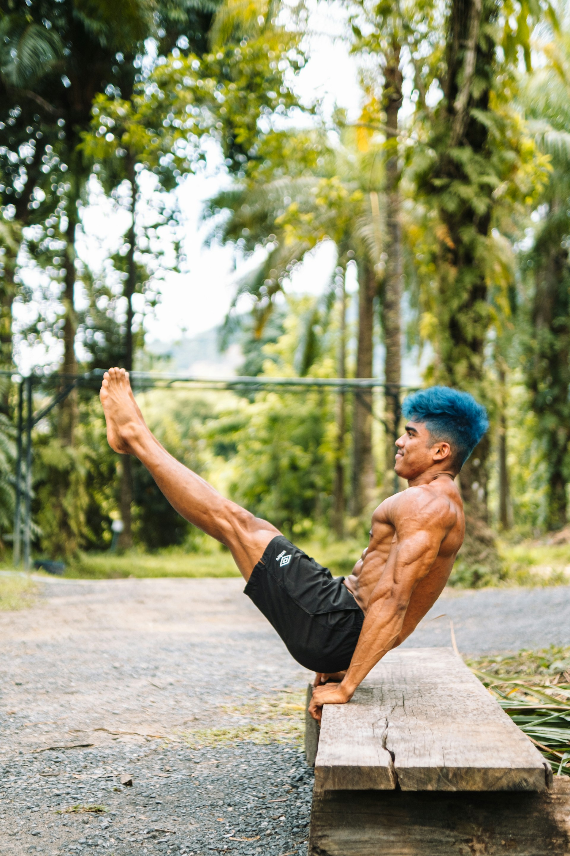 man blue hair exercising on a bench outside by the trees