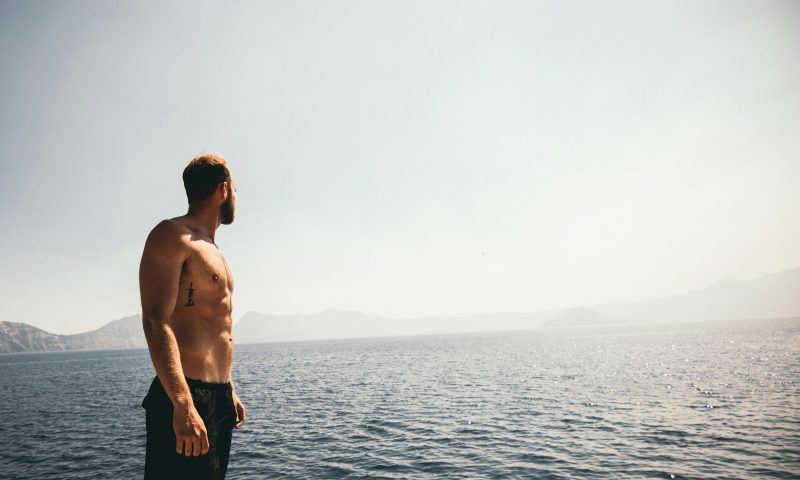 Man with shirt off and strong abs looking over the ocean