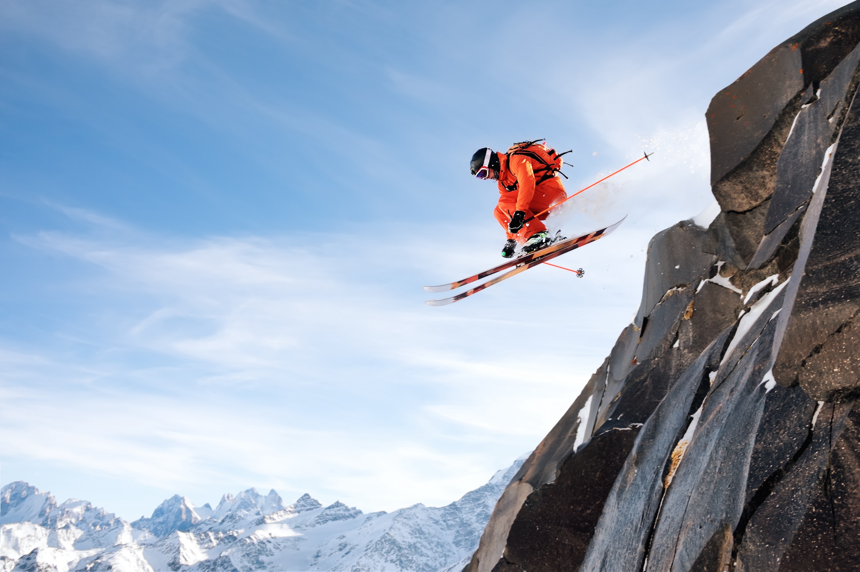 A professional skier makes a jump-drop from a high cliff against the blue sky leaving a trail of snow powder in the mountains. Caucasian ridge in the background. Photo from the slopes of Mount Elbrus. The concept of extreme sports and recreation in the mountains in winter. Copy the space