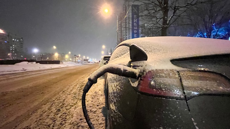 Electric car at night on city charging in snowdrifts. Tesla electric car charging in winter at night.