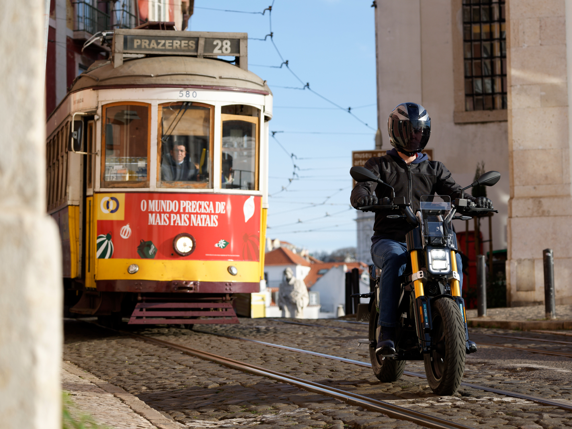 Helmeted rider traveling on a paved city street in front of a red streetcar on a 2024 BMW CE 02,