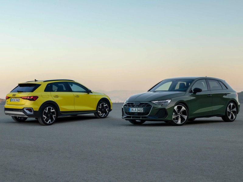 Yellow Audi A3 Allstreet and a green Audi A3 parked on a gray surface with distant hills.