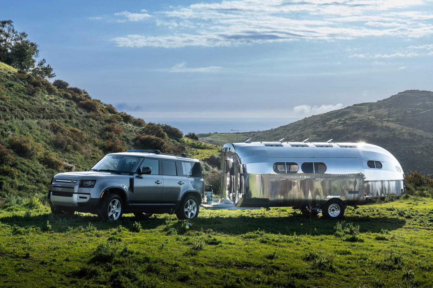 Bowlus Rivet travel trailer being towed by an SUV through a grassy field.