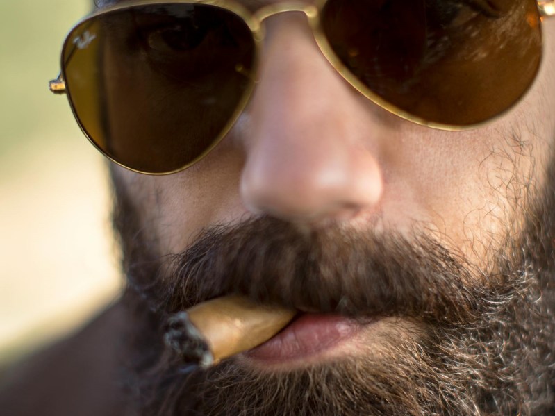 Close up of bearded man smoking a cigar almost done.
