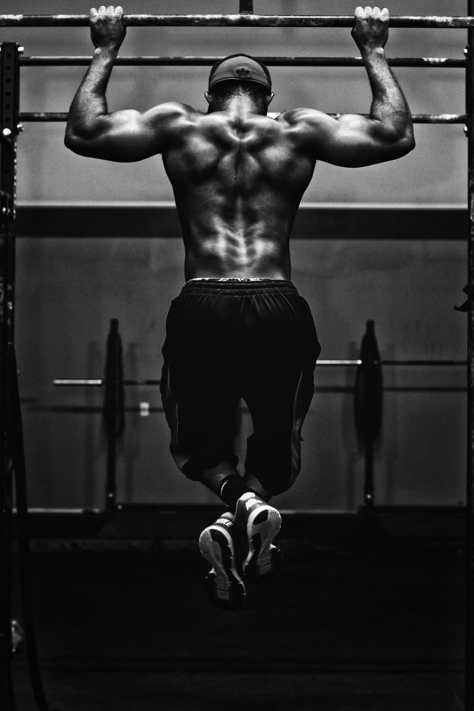 Black and white image of muscular man wearing shorts doing pullup on bar in gym