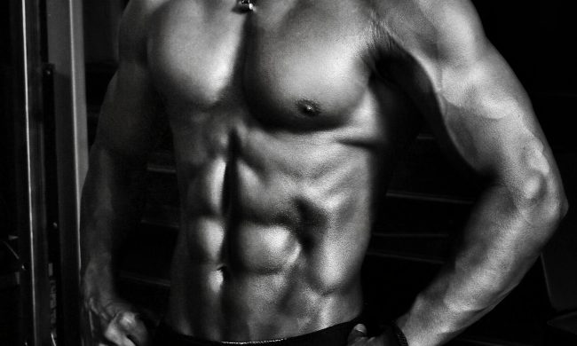 Black and white image of a shirtless man wearing shorts with strong abs on a black background