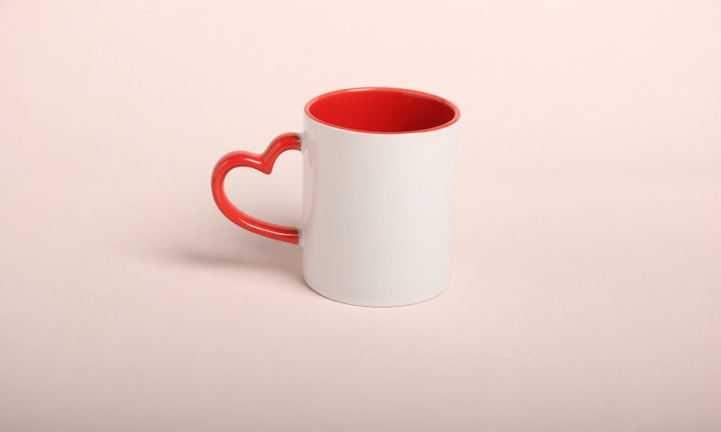 White tea cup or mug with red love heart handle on pink table and background