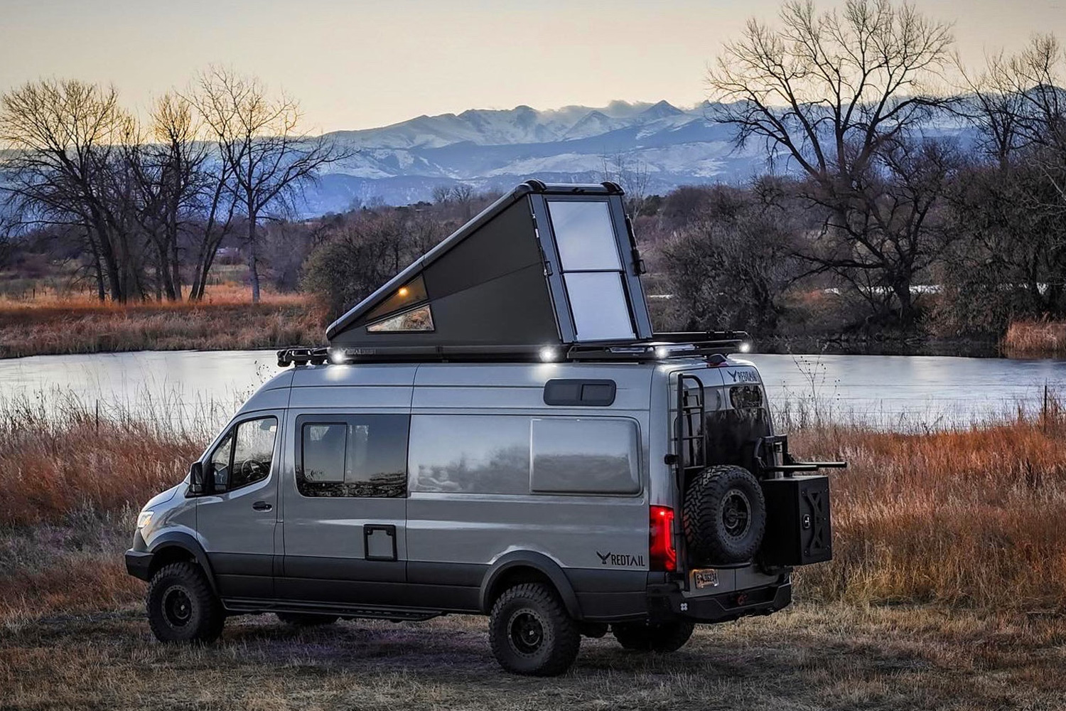 Redtail Overland Skyloft Campervan parked next to a river.