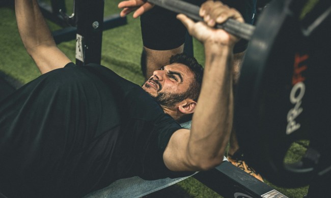 man wearing black shirt laying on bench in gym lifting weights