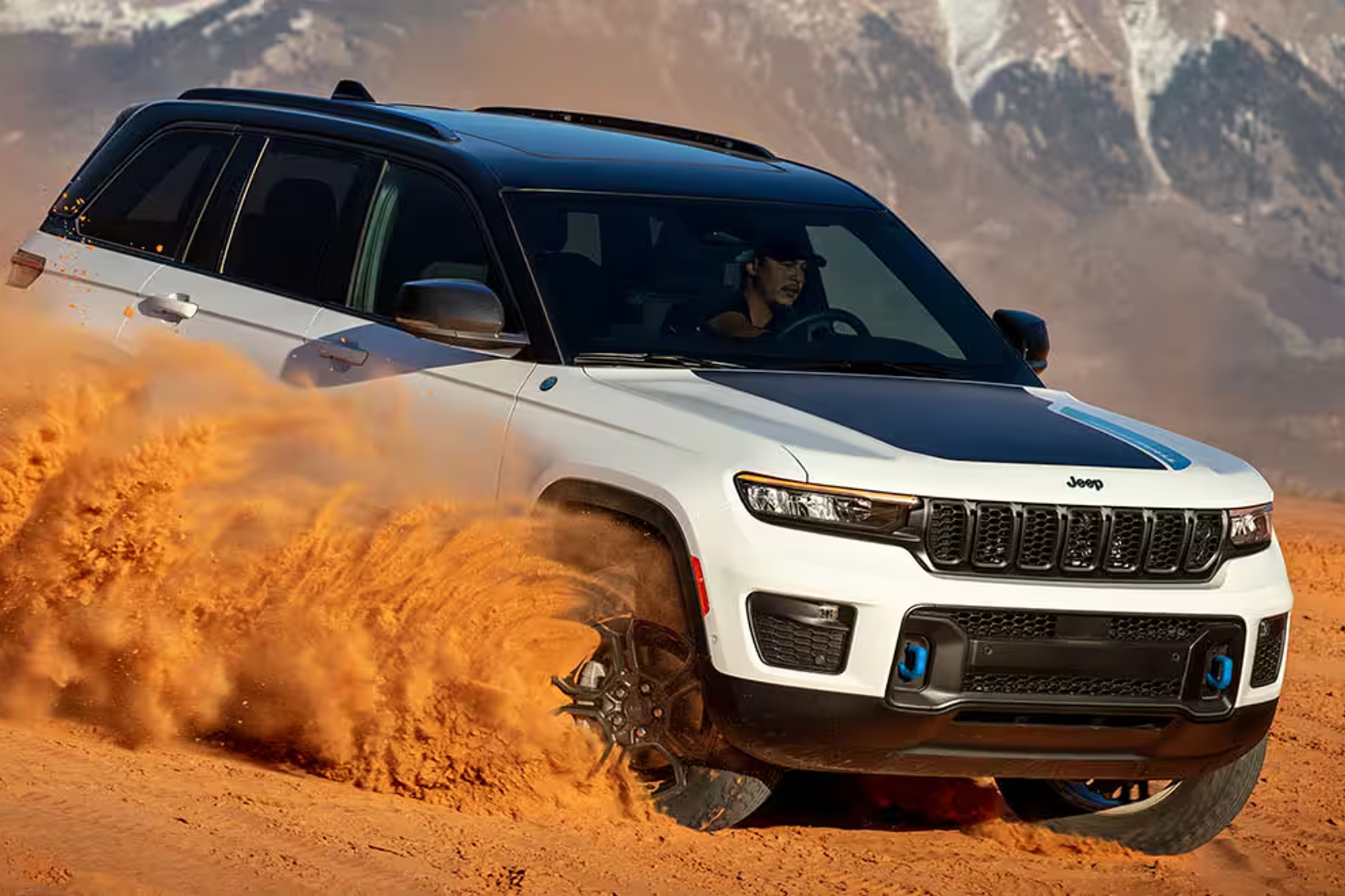electric jeep wrangler 2024 grand cherokee 4xe trailhawk driving hard in desert sand with snow capped mountains the backgroun
