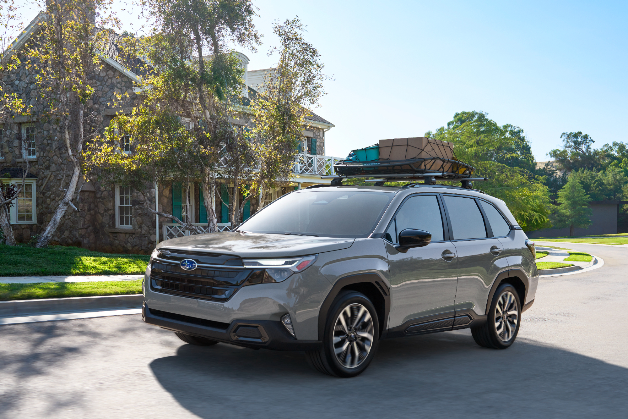 2025 Subaru Forester driving on a neighborhood road past a brick Federal Colonial house.